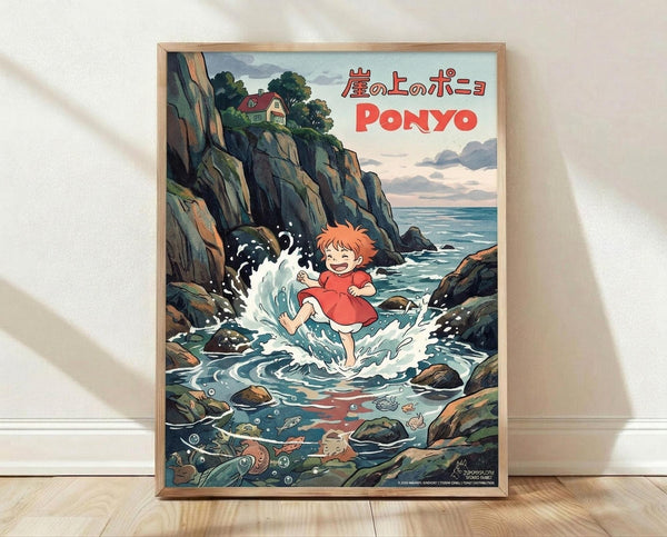 May include: Framed poster print leaning against white wall on light wooden floor. The artwork shows Ponyo, a red-haired character in orange dress, splashing in tidal pool water surrounded by rocky coastal cliffs. Japanese text and "PONYO" title appear at top. Ocean waves crash against dark rocks, with small house visible on clifftop. Rich blues, greens, and earth tones in anime illustration style. Natural wood frame.