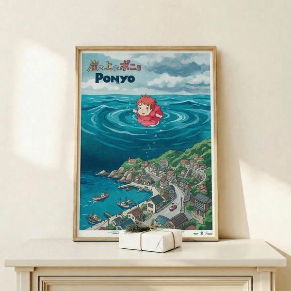 May include: Framed Studio Ghibli Ponyo poster displayed on light wooden shelf against white wall. Artwork shows red-haired Ponyo character floating in ocean waves above coastal Japanese village with traditional buildings and boats. Vibrant blues, greens, and coral colors in anime illustration style. Natural wood frame, small wrapped gift box with twine sits in front. Clean, minimalist home decor setting.