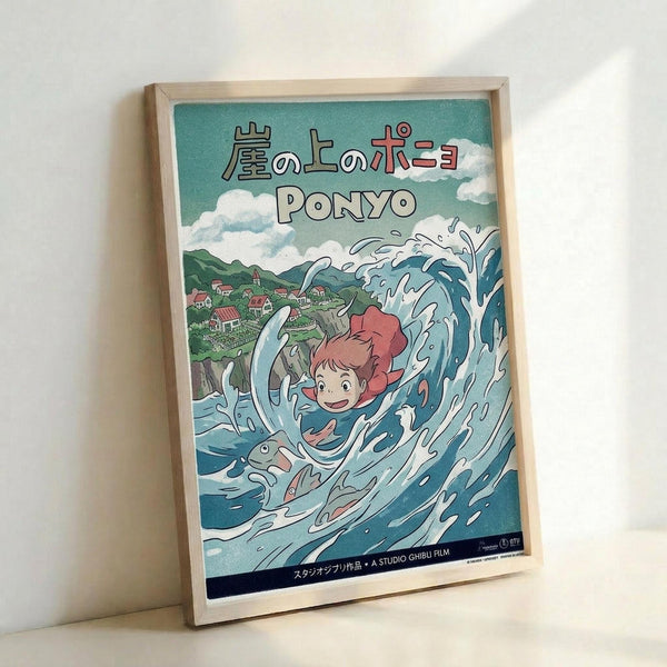 A framed poster showing the animated character Ponyo riding a large blue wave with white foam splashes. The artwork features Japanese text at the top, a small coastal village with green hills in the background, and fluffy white clouds in a turquoise sky. The poster has Studio Ghibli branding at the bottom and is displayed in a light wooden frame leaning against a white wall.