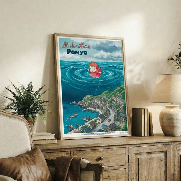 May include: Framed Studio Ghibli Ponyo poster displayed on rustic wooden sideboard in cozy living room setting. Artwork shows red-haired Ponyo character floating in turquoise ocean waters above coastal village scene. Natural wood frame, approximately 16x20 inches, positioned alongside potted fern, ceramic vases, and stacked books. Cream armchair with brown throw pillow visible in foreground against neutral wall backdrop.