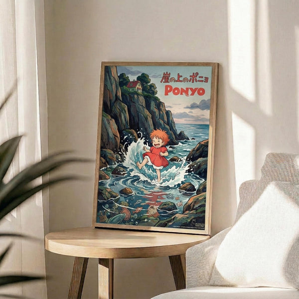 May include: Framed Studio Ghibli Ponyo poster displayed on light wood round side table next to beige upholstered chair. Artwork shows orange-haired child character splashing in ocean waves between rocky coastal cliffs, with Japanese and English text at top. Natural sunlight streams across white walls, with green plant leaves visible in corner.