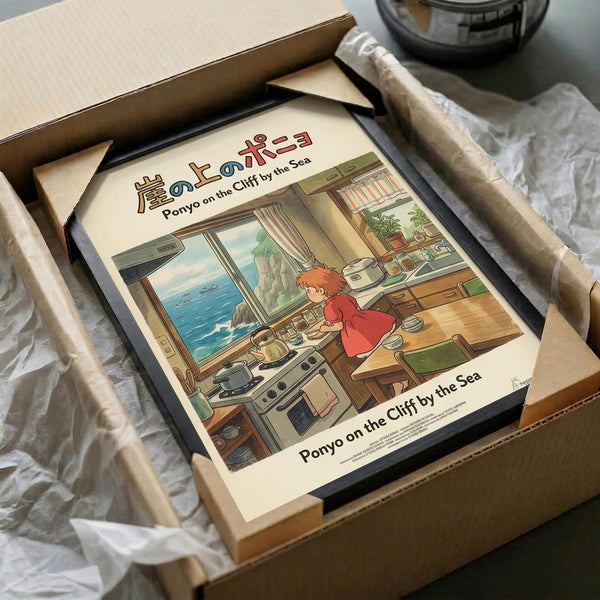 May include: Framed Studio Ghibli poster featuring Ponyo character in red dress cooking in cozy kitchen with ocean view through window. Art print shown in black frame inside cardboard shipping box with protective wrapping materials. Warm-toned illustration depicts detailed kitchen scene with wooden counters, appliances, and seaside cliff landscape visible outside. Japanese and English text at top and bottom of cream-colored poster.