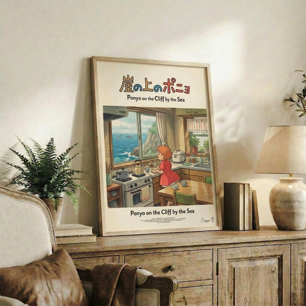May include: Framed Studio Ghibli poster featuring Ponyo character in red dress cooking in cozy kitchen overlooking ocean cliffs, displayed on rustic wooden sideboard with potted fern, ceramic vase, and stack of books in warm, sunlit living room with cream upholstered furniture and neutral walls.