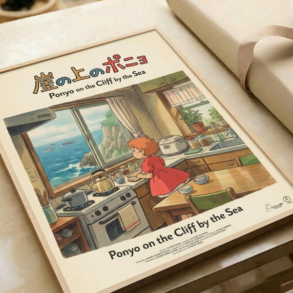 May include: Framed Studio Ghibli poster print featuring Ponyo character in red dress working in a cozy kitchen with ocean view through window. Warm illustrated scene shows wooden counters, cooking equipment, potted plants, and coastal cliffs visible outside. Print has cream matting in light wooden frame, displayed on white bedding surface.