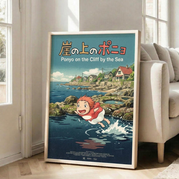 May include: Framed Studio Ghibli Ponyo movie poster displayed in bright living room corner next to beige sofa. Features red-haired character swimming in ocean water with coastal village houses on cliff above. Japanese and English text at top, teal blue background with rocky shoreline. Light wooden frame, poster appears medium to large size leaning against white wall near windows.
