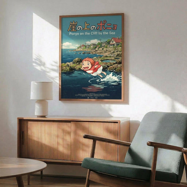 May include: Framed Ponyo on the Cliff by the Sea movie poster displayed above a mid-century modern wooden credenza with table lamp. The poster features the red-haired character Ponyo splashing in blue water with a coastal village backdrop. Room has white walls, natural lighting, and a teal upholstered chair with wooden arms visible in corner.