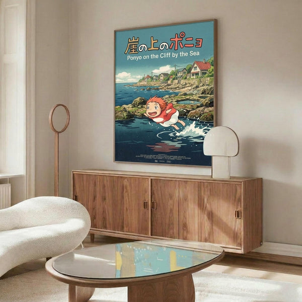 May include: Studio Ghibli-style poster mounted on beige wall above wooden credenza in modern living room. Poster shows red-haired boy swimming in blue ocean water near coastal cliffs with houses, featuring Japanese and English text. Room has white curved chair, glass coffee table, floor lamp, and minimalist mid-century decor with warm wood tones and neutral colors.
