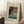 May include: Framed vintage Japanese woodblock print showing people in a boat on blue water near a thatched-roof house, with "Enjoying Evening Cool" text and dates 1926-1927. Print has cream matting in light wood frame, leaning against white wall next to white coffee cup on wooden block and beige knit blanket on white textured rug.