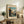May include: Vintage Japanese woodblock-style poster featuring Mount Fuji viewed through autumn trees and rocky stream, displayed in light wood frame on rustic wooden console with fern plant, ceramic lamp, pottery vase and leather furniture in neutral-toned living room setting