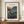 May include: Framed vintage Japanese woodblock print featuring traditional houses nestled among trees and rocky cliffs at twilight, with mountain silhouettes in background. Warm peachy-pink sky contrasts with deep blue hills. Print displays "HAKONE 1939" at top and artist signature below. Wooden frame sits on walnut credenza beside white ceramic vase and stacked books against cream walls with white trim molding.