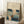 May include: Framed Japanese woodblock print poster showing boats with white sails on blue water under a twilight sky, displayed in light wooden frame leaning against white wall corner next to textured throw blanket and wooden side table with white coffee cup, creating cozy bedroom or living room setting with natural window lighting.