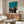 May include: Japanese art poster with turquoise background showing black silhouettes of dancing figures in traditional clothing, displayed above a mid-century modern walnut credenza. White mushroom table lamp and brass floor lamp beside cream curved chair with glass oval coffee table in bright, minimalist living room setting.