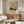 May include: Vintage Japanese art poster featuring Mount Fuji with snow-capped peak against orange sunset sky, displayed in thin brown frame on white wall above mid-century walnut credenza. Modern living room setting with white curved lounge chair, glass oval coffee table, and white mushroom table lamp. Warm wood tones throughout minimalist Scandinavian-style interior with natural lighting.
