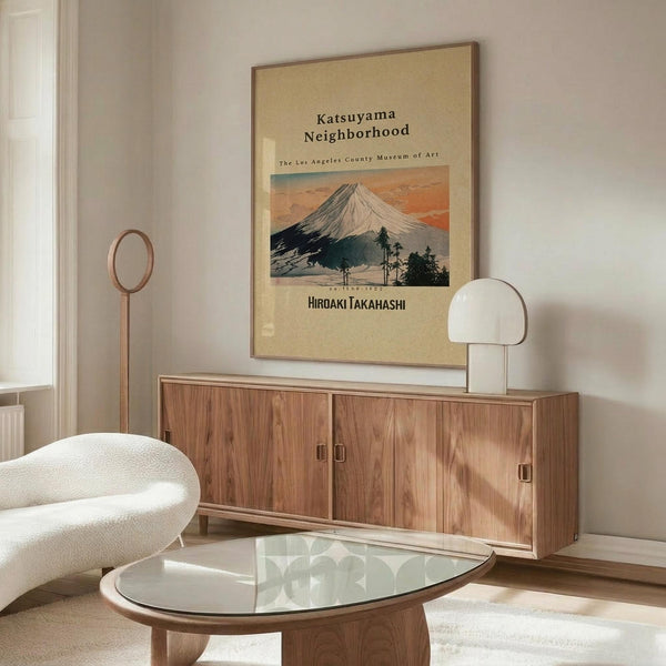 May include: Vintage Japanese art poster featuring Mount Fuji with snow-capped peak against orange sunset sky, displayed in thin brown frame on white wall above mid-century walnut credenza. Modern living room setting with white curved lounge chair, glass oval coffee table, and white mushroom table lamp. Warm wood tones throughout minimalist Scandinavian-style interior with natural lighting.