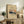May include: Framed vintage Japanese art print featuring Mount Fuji with snow-capped peak against orange sunset sky, displayed on rustic wooden console table alongside fern plant, books, and ceramic vase in neutral-toned living room setting with cream upholstered chair and white walls