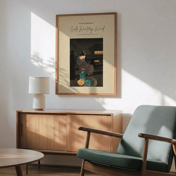 May include: Japanese woodblock print poster in wooden frame hanging above mid-century modern credenza with ceramic lamp. Green upholstered armchair with wood frame sits nearby. Print shows figure in dark robes with colorful pottery vessels. Warm sunlight creates shadows across white wall. Room has minimalist aesthetic with natural wood tones.