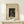 May include: Framed vintage Japanese woodblock print poster displayed on light wood shelf against cream wall. Features woman in dark kimono with teal accents sitting by wooden structure. Museum exhibition poster style with beige matting in natural wood frame. Small white wrapped gift with greenery sits beside frame.