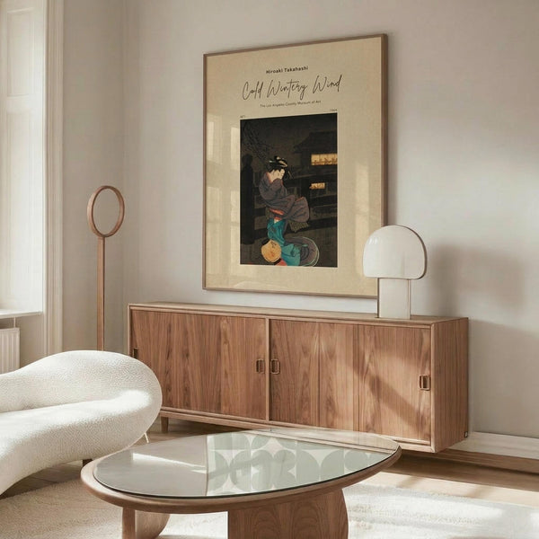 May include: Japanese woodblock print poster in beige mat and thin frame, hanging above modern walnut credenza in minimalist living room. Print shows woman in traditional dress sitting by wooden structure. White sculptural chair, glass oval coffee table, and spherical table lamp visible. Warm wood tones throughout neutral-colored space with natural lighting.