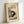 May include: Framed vintage Japanese art print showing a black and white cat sitting beneath a tomato plant with red tomatoes and green leaves. The artwork has a cream background with Japanese characters and "HIROAKI TAKAHASHI 1931" text at bottom. Light wood frame displayed against white wall, casting soft shadows.