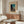 May include: Framed vintage Japanese woodblock print poster showing figure at dusk in teal and orange tones, displayed above wooden mid-century sideboard in minimalist living room with white sculptural chair, glass coffee table, and modern table lamp