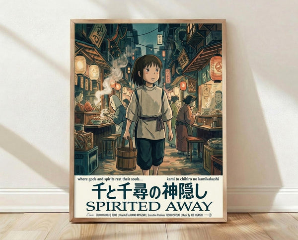 May include: Framed Spirited Away movie poster showing young Chihiro holding a wooden bucket in a bustling Japanese bathhouse street scene with glowing red lanterns, traditional wooden buildings, and various characters. The anime-style artwork features warm earth tones and vintage aesthetic. Japanese and English text appears at bottom. Light wood frame leans against white wall on wooden floor with soft natural lighting creating shadows.