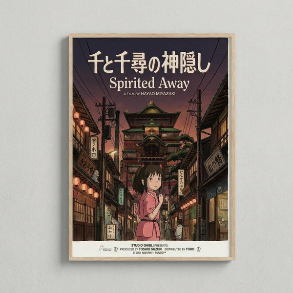 May include: Framed poster of animated film artwork showing a young girl in pink shirt standing on a traditional Japanese street at dusk. The scene features multi-story buildings with green roofs, glowing red lanterns, and Japanese signage. The poster has a light wooden frame and hangs on a white textured wall, displaying both Japanese and English text at the top.