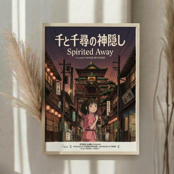 May include: Framed Spirited Away movie poster in light wood frame hanging on white wall next to dried pampas grass. Poster shows anime girl in pink outfit walking through traditional Japanese street with lanterns, shops, and pagoda building in background. Artwork features rich purples, warm lighting, and detailed architectural elements in Studio Ghibli's distinctive animation style.
