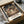 May include: Framed Spirited Away poster print featuring Chihiro standing on wooden steps in a magical Japanese bathhouse town at night, with traditional architecture and glowing lanterns. The vintage-style print is shown in a black frame inside an unboxed cardboard package with tissue paper wrapping, displayed on a white cloth surface.
