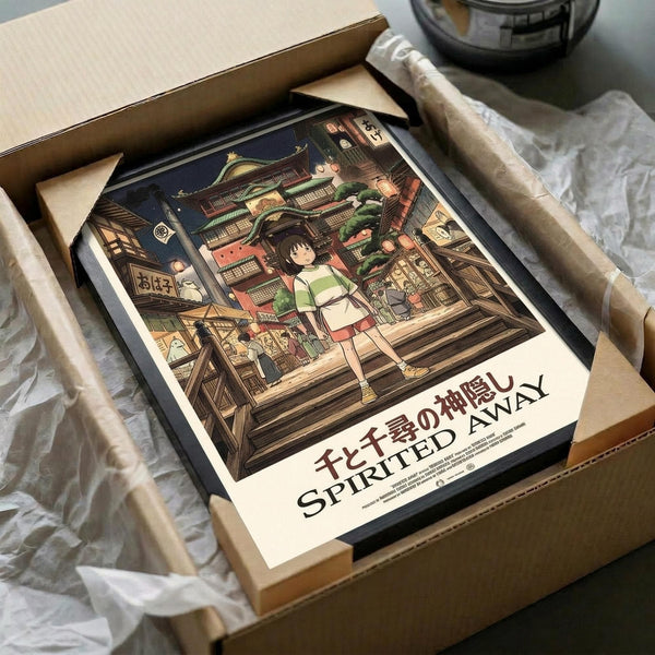 May include: Framed Spirited Away poster print featuring Chihiro standing on wooden steps in a magical Japanese bathhouse town at night, with traditional architecture and glowing lanterns. The vintage-style print is shown in a black frame inside an unboxed cardboard package with tissue paper wrapping, displayed on a white cloth surface.