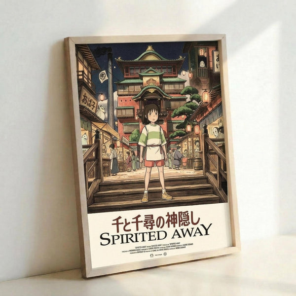 A framed poster featuring the animated character Chihiro standing on wooden steps in a traditional Japanese town setting. The artwork shows detailed architecture with a multi-story bathhouse building featuring green roofs and traditional design elements. The scene is set at dusk with lanterns glowing throughout the village streets. Below the colorful illustration, the title appears in both Japanese characters and English text reading "Spirited Away." The poster is displayed in a light wooden fra