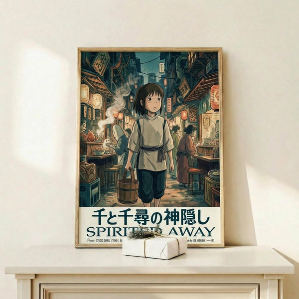 May include: Framed Spirited Away movie poster displayed on light wood shelf against white wall. Features young girl character Chihiro in traditional clothing walking through bustling Japanese street scene with lanterns, food stalls, and other characters. Artwork shows Studio Ghibli's distinctive animation style with rich greens, blues, and warm lighting. Small white decorative box sits beside the wooden-framed print on the minimalist shelf.
