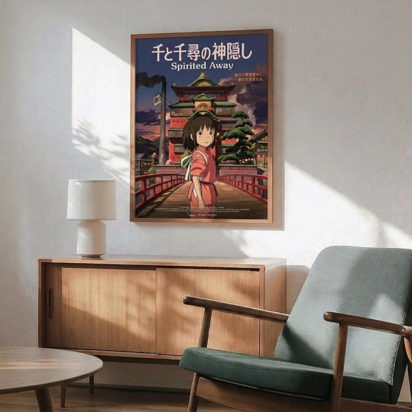 May include: Framed Studio Ghibli Spirited Away movie poster hanging on white wall above wooden sideboard with ceramic lamp. Poster shows anime girl in red outfit standing on wooden bridge before ornate Japanese bathhouse building against twilight sky. Mid-century modern room setting with teal upholstered armchair, round wooden coffee table, and natural sunlight casting geometric shadows across the scene.