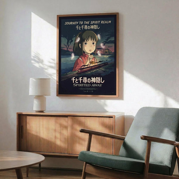 May include: Framed Spirited Away movie poster hanging on white wall above wooden sideboard with lamp and green upholstered chair. Poster features anime girl with dark hair in red clothing against twilight scene with train and spirits. Warm natural lighting creates shadows across minimalist room setting.