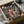 May include: Framed Spirited Away movie poster featuring anime character Chihiro in red outfit against fantastical bathhouse landscape, nestled in cardboard shipping box with protective tissue paper wrapping, warm lighting creates cozy unboxing scene