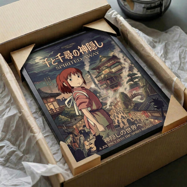 May include: Framed Spirited Away movie poster featuring anime character Chihiro in red outfit against fantastical bathhouse landscape, nestled in cardboard shipping box with protective tissue paper wrapping, warm lighting creates cozy unboxing scene
