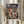 May include: Person in cream clothing holding framed Spirited Away movie poster featuring red-haired girl character against backdrop of Japanese buildings and bathhouse. Golden frame, dried pampas grass visible on left side. Soft natural lighting creates shadows on neutral wall background.