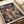 May include: Spirited Away anime poster print featuring Chihiro in traditional Japanese clothing against a fantastical bathhouse landscape with swirling clouds and architectural details. The artwork displays rich earth tones and Studio Ghibli's distinctive animation style. Shown as a flat print on white paper with soft lighting, alongside rolled paper tubes suggesting packaging materials.