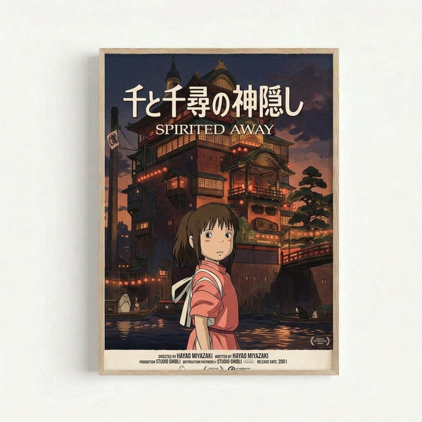 Framed movie poster featuring an anime girl with brown hair wearing a red and white striped shirt, standing before a large ornate Japanese bathhouse building with multiple levels, traditional architecture, and glowing lanterns. The scene has a twilight sky with purple and orange hues reflecting on water below. Japanese text appears at the top with "SPIRITED AWAY" underneath in English. The poster is displayed in a light wooden frame against a white wall.