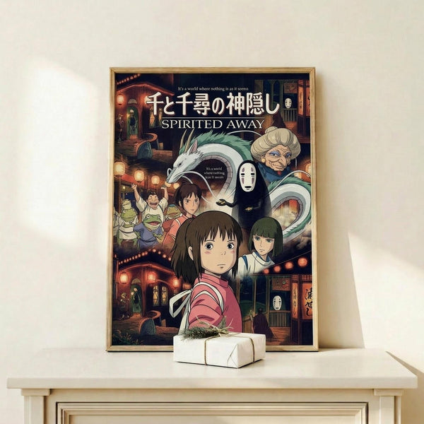 May include: Framed Spirited Away movie poster featuring main character Chihiro in pink kimono surrounded by animated characters including No-Face, Haku the dragon, and Zeniba, displayed on light wood shelf with small wrapped gift, against cream wall with natural lighting