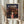May include: Hands holding a framed Spirited Away movie poster featuring the young girl Chihiro in a pink shirt standing before an illuminated traditional Japanese bathhouse at twilight. The poster has Japanese text at the top with "Spirited Away" below, set in a light wood frame. Dried wheat stalks visible on the left side, neutral curtained background.