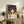 May include: Framed Spirited Away movie poster featuring anime character Chihiro with short brown hair and green shirt, surrounded by white spirits against mystical bathhouse background. Japanese and English text below. Wooden frame displayed on rustic dresser with plant, books, and ceramic vases in modern living room setting.
