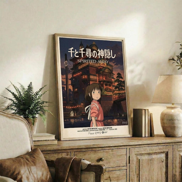 May include: Framed Spirited Away movie poster featuring young girl in red striped shirt against twilight bathhouse backdrop, displayed on rustic wooden sideboard alongside fern plant, books, and ceramic vase in cozy living room with beige armchair and neutral decor