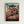 May include: Framed anime movie poster mounted on white wall. Features young girl in pink outfit leaping through air above traditional Japanese bathhouse with curved green roofs. Red bridge spans foreground, industrial smokestack visible left side. Artwork shows detailed architectural elements, cloudy sky backdrop in warm sunset tones. Natural wood frame surrounds colorful illustration with Japanese text and English subtitle at bottom.