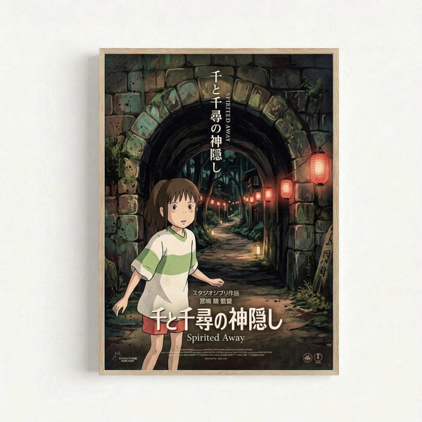Studio Ghibli movie poster featuring young girl Chihiro in green and white striped shirt standing before a stone archway tunnel with glowing red lanterns. Dark atmospheric scene with moss-covered stones and mysterious pathway leading into shadows. Japanese text at top, "Spirited Away" title at bottom. Framed in light wood frame against white wall.