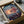 May include: Framed poster of animated girl in pink kimono running across wooden dock at sunset, displayed in cardboard shipping box with protective packaging. Colorful artwork shows water reflections and cloudy sky in anime style. Black frame sits nestled in brown cardboard with white tissue paper padding around edges.