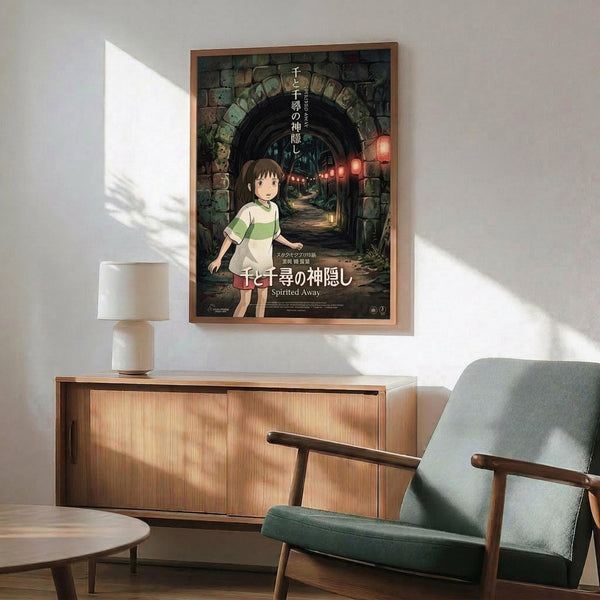 May include: Framed Spirited Away movie poster hanging on white wall above wooden sideboard with table lamp. Green upholstered armchair with wooden arms sits nearby. Poster shows young girl character standing in stone archway tunnel with red lanterns, featuring Japanese text and "Spirited Away" title. Warm sunlight streams across minimalist room with mid-century modern furniture.
