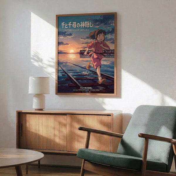 May include: Framed Spirited Away movie poster mounted on white wall above wooden sideboard with table lamp. Shows animated girl character running on wooden planks over water at sunset with Japanese text and "Spirited Away" title. Natural wood frame matches mid-century modern furniture including sage green upholstered armchair. Warm sunlight creates shadows across minimalist living room setting.