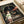 May include: A vintage-style movie poster featuring an animated young girl with brown hair in a green and white striped shirt, standing in front of a stone archway tunnel with glowing red lanterns. The poster displays Japanese text and "Spirited Away" in English at the bottom. The print is shown laying flat on white paper with a cream ribbon visible in the corner, creating an unboxing or gift presentation scene.
