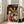 May include: Framed anime movie poster leaning against white wall next to beige sofa in bright living room. Poster shows young girl in pink shirt looking back at crowded scene of colorful spirits and creatures in lantern-lit traditional Japanese street. Japanese and English text at top. Light wooden frame, approximately 2-3 feet tall based on furniture scale.