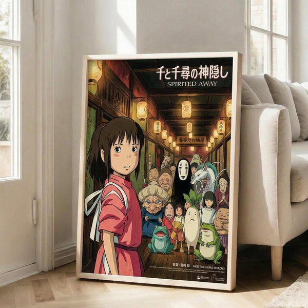 May include: Framed anime movie poster leaning against white wall next to beige sofa in bright living room. Poster shows young girl in pink shirt looking back at crowded scene of colorful spirits and creatures in lantern-lit traditional Japanese street. Japanese and English text at top. Light wooden frame, approximately 2-3 feet tall based on furniture scale.